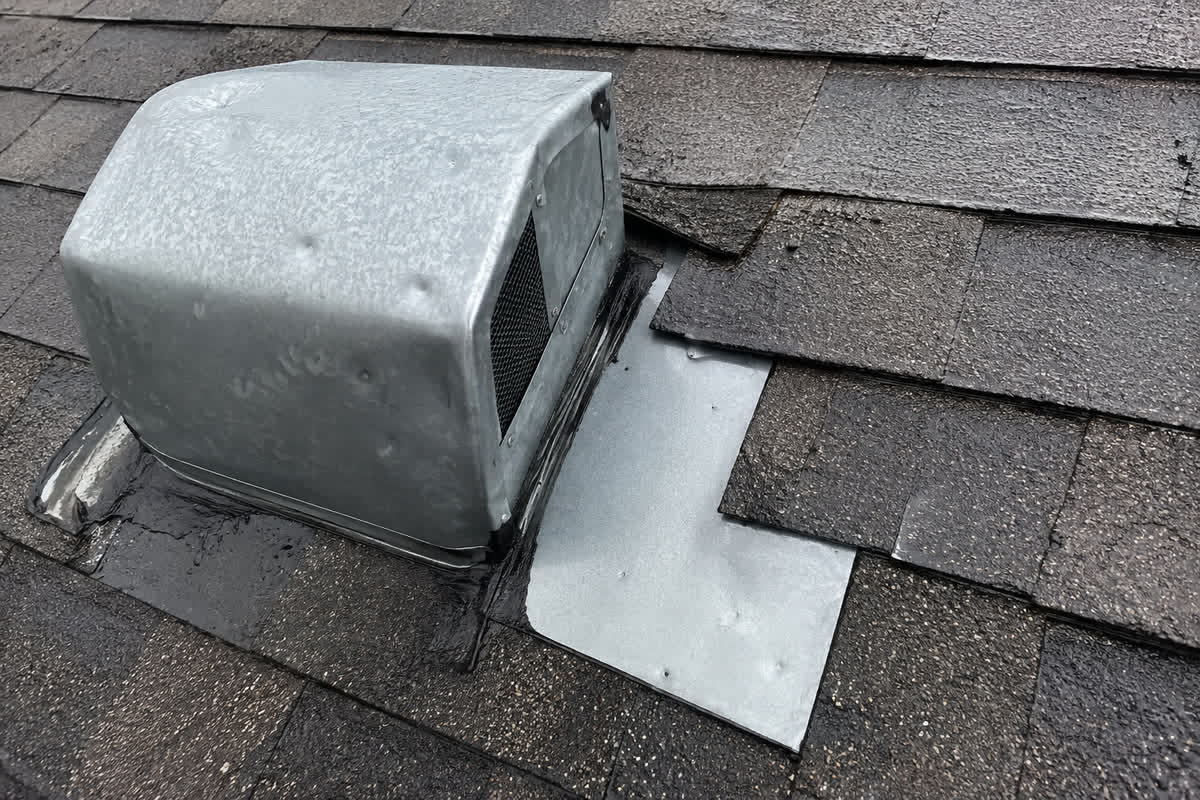 Illustration of small hail dents on a galvanized roof vent and flashing beside asphalt shingles
